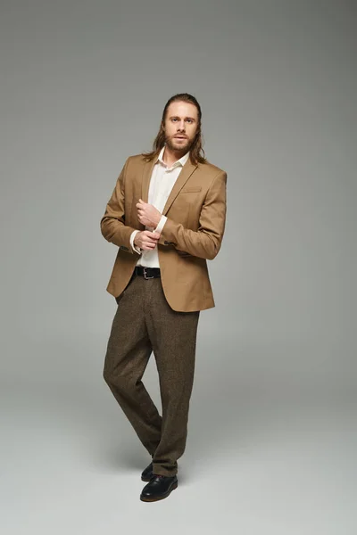 Handsome businessman with beard and long hair posing in blazer on grey backdrop, formal attire — Stock Photo