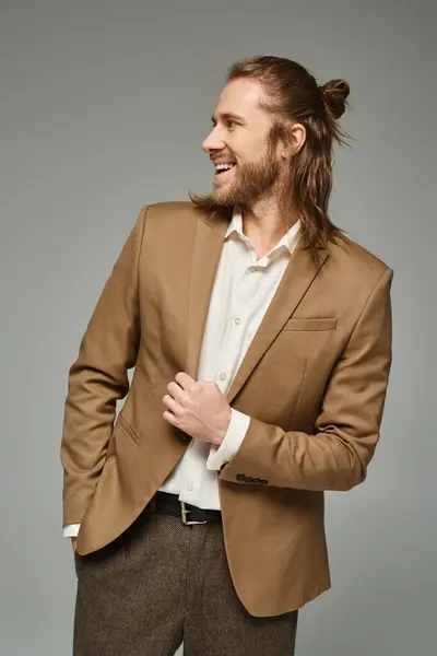 Allegro uomo d'affari con barba e capelli lunghi in posa in blazer su sfondo grigio, abbigliamento formale — Foto stock