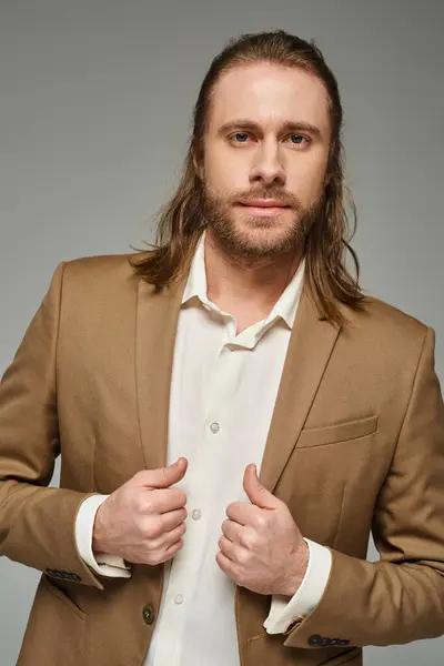Gutaussehender Geschäftsmann mit Bart und langen Haaren, der im Blazer vor grauem Hintergrund posiert, formelle Kleidung — Stockfoto
