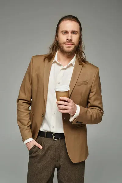 Gutaussehender Geschäftsmann mit Bart und langen Haaren, der Kaffee hält, um auf grauem Hintergrund zu gehen, formelle Kleidung — Stockfoto