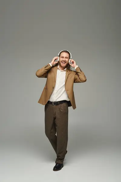 Cheerful bearded businessman in headphones listening music on grey backdrop, formal attire — Stock Photo