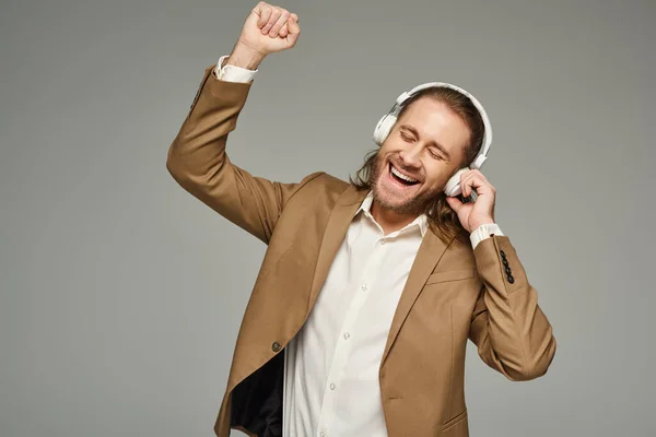 Здивований бородатий бізнесмен в навушниках, слухаючи музику на сірому фоні, формальний одяг — стокове фото