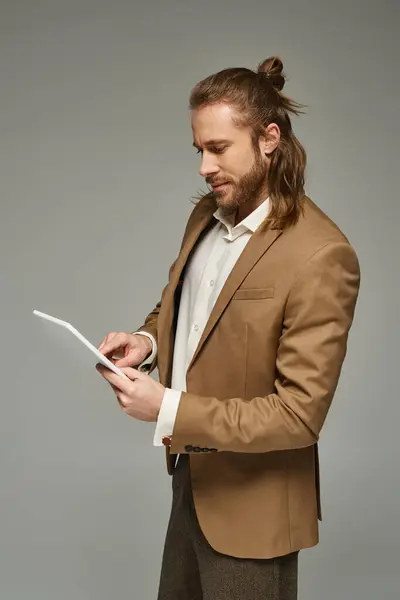 Bearded businessman with long hair posing in formal attire and using digital tablet on grey backdrop — Stock Photo