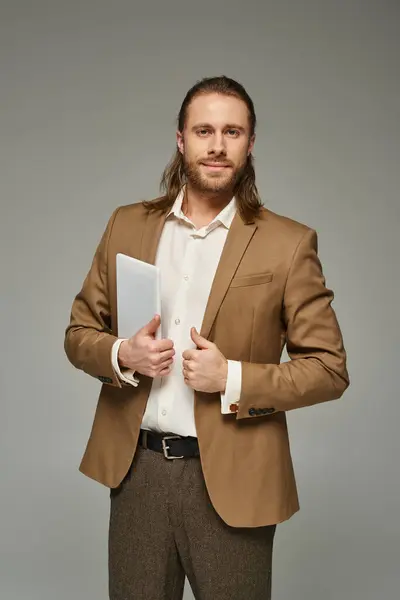 Бородатий бізнесмен з довгим волоссям позує в офіційному вбранні і використовує цифровий планшет на сірому фоні — стокове фото