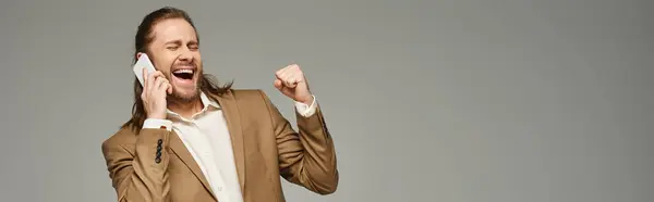 Bonito e animado barbudo empresário em traje formal falando no smartphone em cinza, banner — Fotografia de Stock