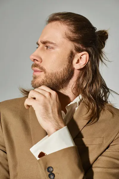 Портрет красивого бизнесмена с длинными волосами и бородой, позирующего в бежевом блейзере на сером фоне — стоковое фото