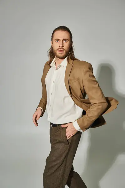 Handsome businessman with long hair and beard posing with hand in pocket on grey background — Stock Photo