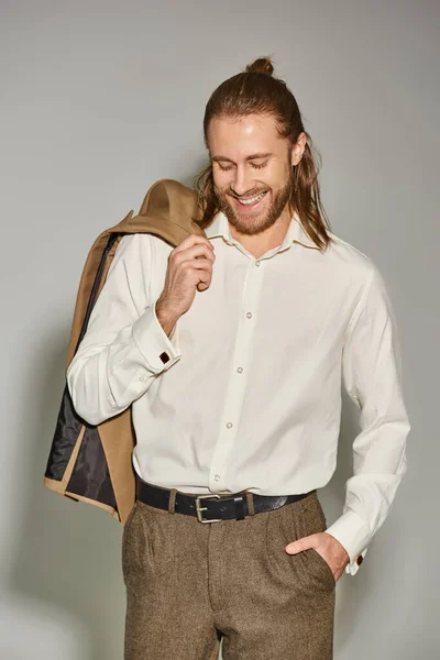 Homem de negócios positivo e barbudo em camisa branca posando com blazer bege no ombro no cinza — Fotografia de Stock