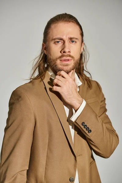 Retrato de hombre de negocios pensativo y atractivo en camisa blanca y chaqueta beige sobre fondo gris - foto de stock