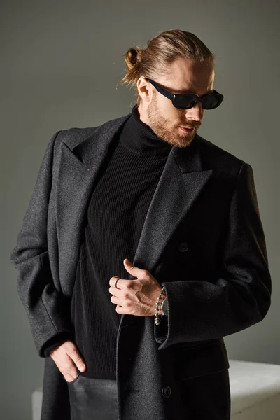 Portrait of fashionable man in trendy sunglasses and woolen coat posing on grey background — Stock Photo