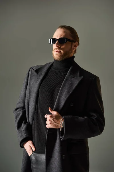 Ritratto di uomo alla moda in occhiali da sole alla moda e cappotto in posa con mano in tasca su grigio — Foto stock