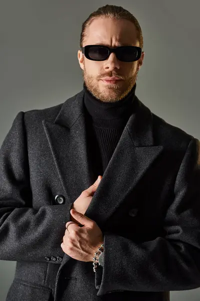 Portrait of handsome male model in trendy sunglasses and black attire standing on grey backdrop — Stock Photo