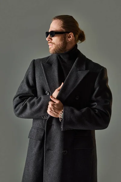 Portrait of handsome male model in trendy sunglasses and black attire looking away on grey backdrop — Stock Photo