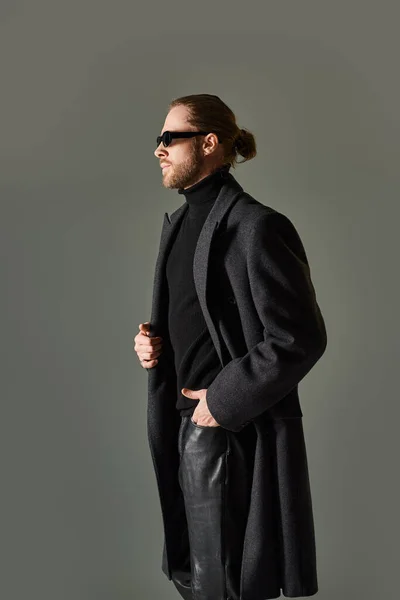 Retrato de guapo modelo masculino en gafas de sol de moda y traje negro posando con la mano en el bolsillo - foto de stock