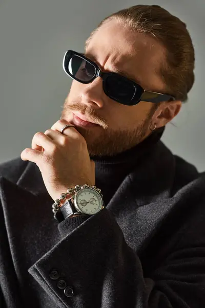 Pensive and bearded man in trendy dark sunglasses and black attire posing on grey background — Stock Photo