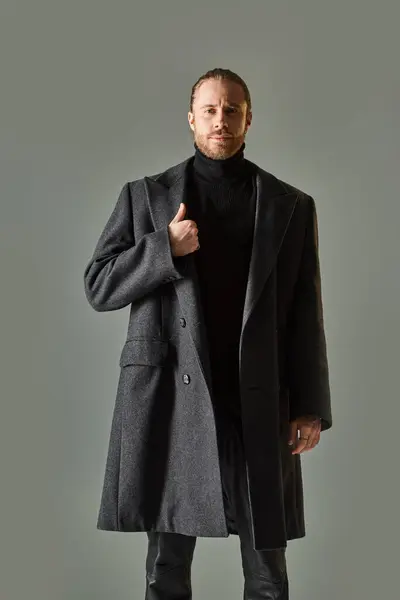 Bello e barbuto uomo in abito nero alla moda e cappotto di lana in posa su sfondo grigio — Foto stock