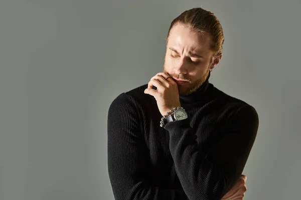 Thoughtful man in turtleneck sweater holding hand near chin and posing on grey background — Stock Photo