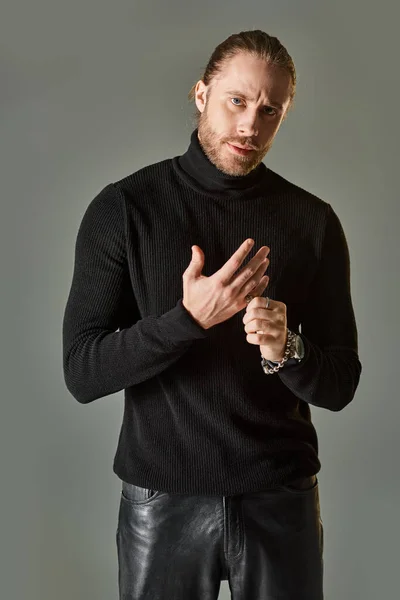 Schöner bärtiger Mann in schwarzem Rollkragenpullover mit silbernem Ring am Finger auf grauem Hintergrund — Stockfoto