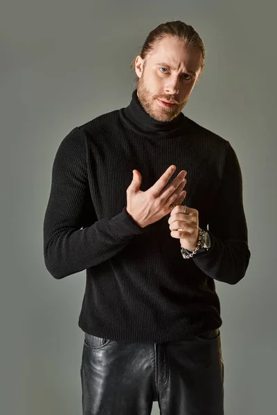 Handsome bearded man in black turtleneck sweater wearing silver ring on finger on grey background — Stock Photo