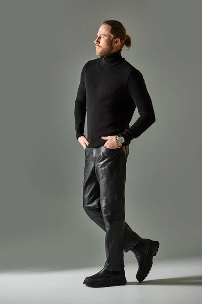 Handsome bearded man in black turtleneck sweater and leather pants posing on grey background — Stock Photo
