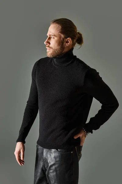 Bonito barbudo homem no preto gola alta camisola e calças de couro posando no fundo cinza — Fotografia de Stock