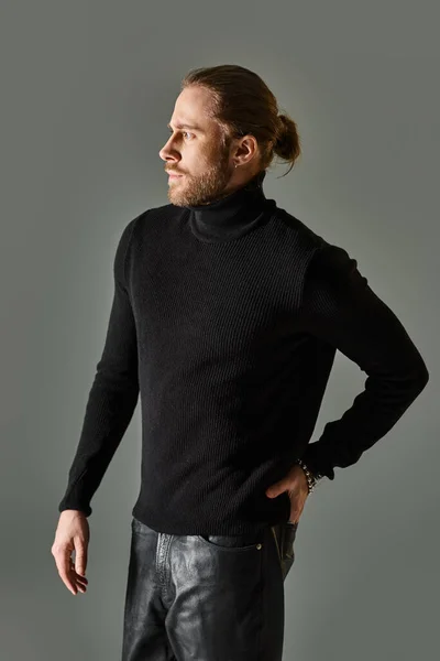 Handsome bearded man in black turtleneck sweater and leather pants posing on grey background — Stock Photo