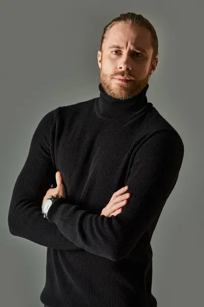 Retrato de hombre guapo en jersey de cuello alto negro posando con los brazos cruzados sobre fondo gris - foto de stock