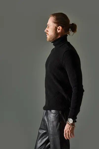 Вид сбоку на красивого мужчину в свитере с водолазкой и кожаных штанах, позирующих на сером фоне — стоковое фото