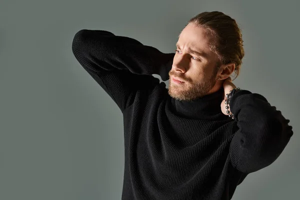 Portrait of handsome man in turtleneck sweater posing with hands behind neck on grey backdrop — Stock Photo