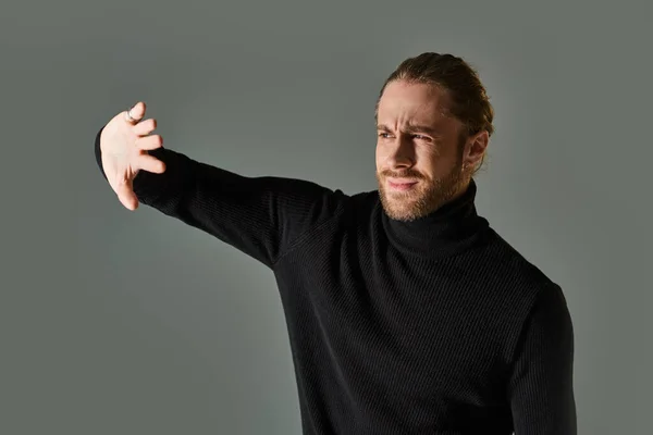 Retrato de homem descontente em camisola gola alta posando com as mãos perto do rosto em pano de fundo cinza — Fotografia de Stock