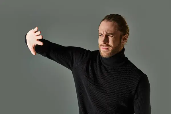 Retrato del hombre disgustado en jersey de cuello alto posando con las manos cerca de la cara sobre fondo gris - foto de stock