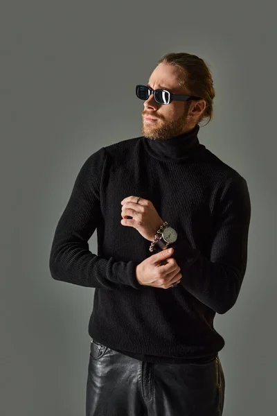 Bearded man in trendy sunglasses, turtleneck sweater and black leather pants posing on grey — Stock Photo