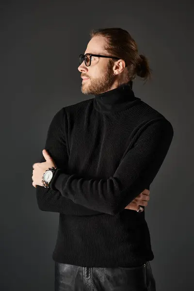 Uomo barbuto in maglione collo alto nero e occhiali in piedi e guardando lontano su sfondo grigio — Foto stock