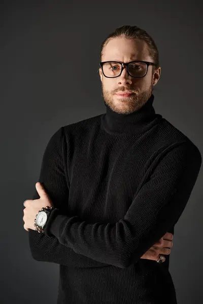 Bearded man in black turtleneck sweater and eyeglasses standing with crossed arms on grey background — Stock Photo