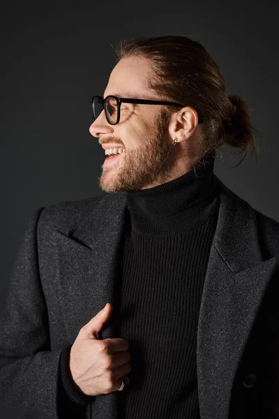 Homme gai dans des lunettes et manteau de laine chic riant et regardant loin sur fond gris — Photo de stock