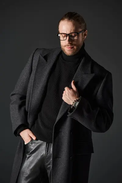 Красивий чоловік в окулярах і стильне вовняне пальто позує рукою в кишені на сірому фоні — стокове фото
