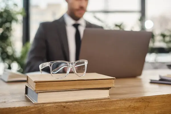 Selective focus of eyeglasses on books near blurred cropped businessman working on laptop in office — Stock Photo