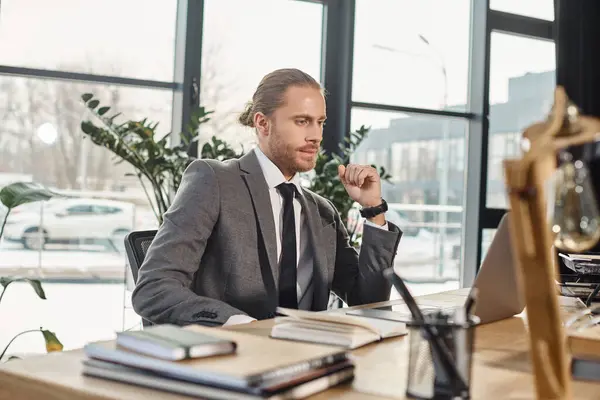 Thoughtful businessman in formal wear looking at laptop while sitting at workplace in modern office — Stock Photo