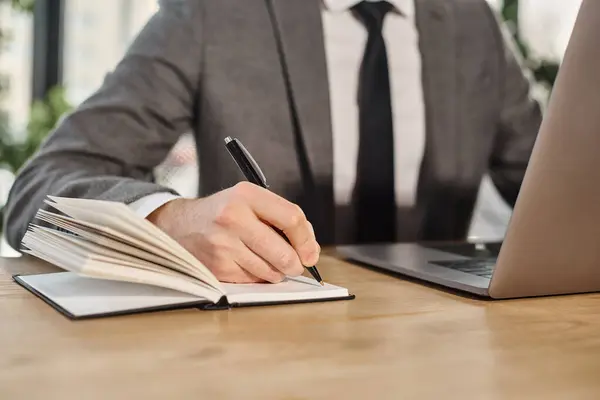 Vue recadrée d'un homme d'affaires en tenue formelle écrivant dans un cahier assis sur le lieu de travail au bureau — Photo de stock