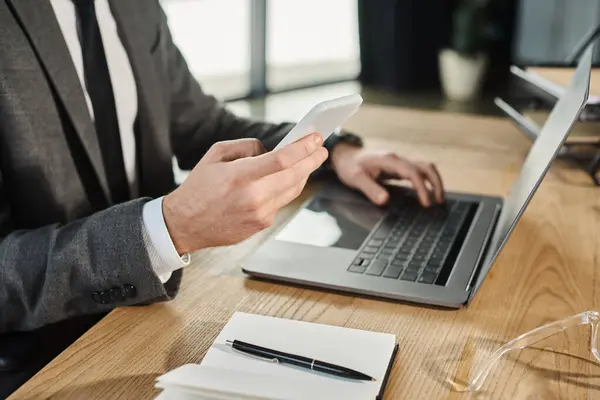 Visão cortada de homem de negócios com smartphone perto de laptop e notebook na mesa de trabalho no escritório — Fotografia de Stock