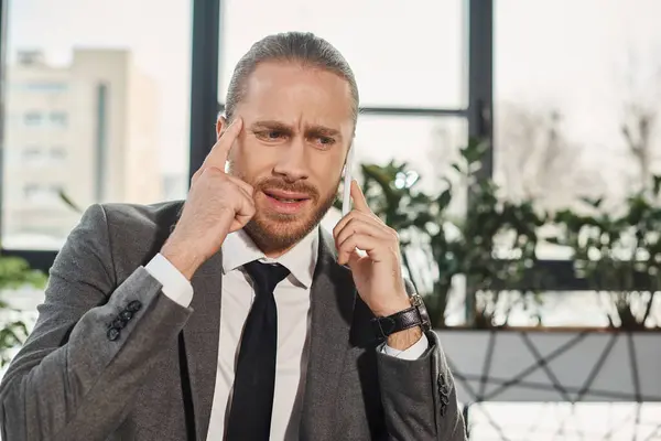 Thoughtful worried businessman touching head and talking on smartphone in office, problem solving — Stock Photo