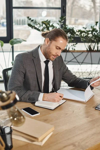 Homme d'affaires concentré en tenue formelle travaillant avec des ordinateurs portables près du smartphone avec écran vierge — Photo de stock