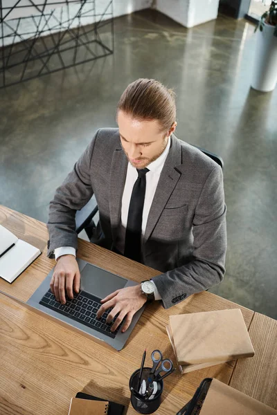 Top view of manager in grey suit typing on laptop near notebooks on work desk in modern office — Stock Photo