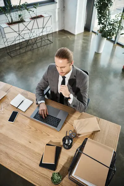 Top view of businessman in formal wear typing on laptop near smartphone and notebooks on work desk — Stock Photo