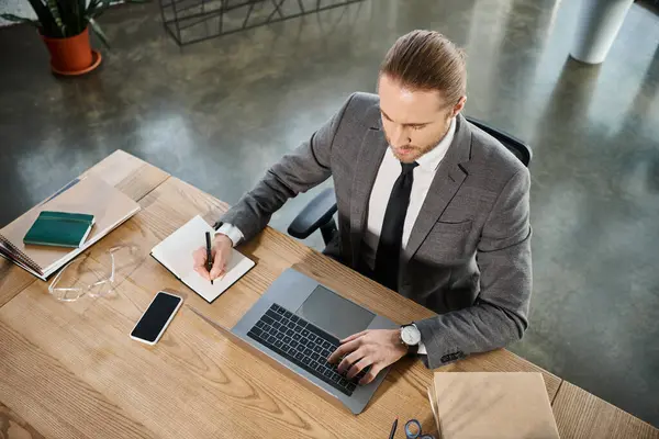 Busy businessman in typing on laptop and writing in notebook near smartphone on work desk, top view — Stock Photo
