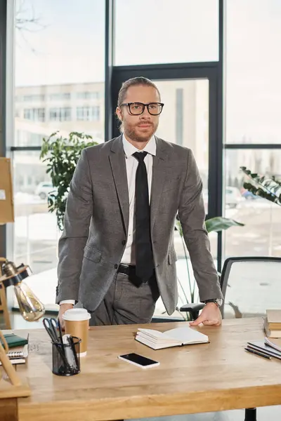 Uomo d'affari serio ed elegante in occhiali in piedi sul posto di lavoro in ufficio e guardando altrove — Foto stock