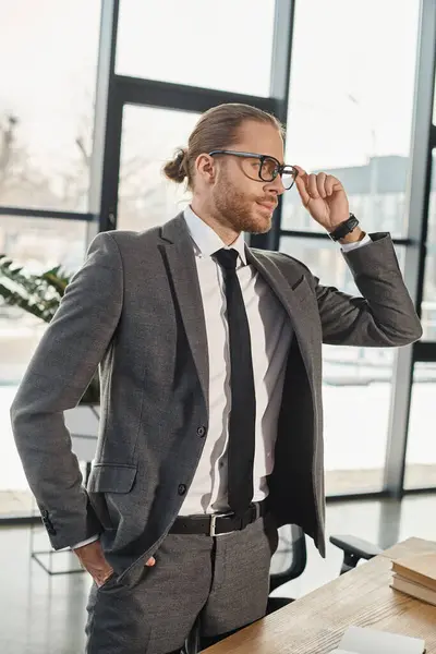 Fiducioso manager aziendale in occhiali in piedi con la mano in tasca e guardando altrove in ufficio — Foto stock