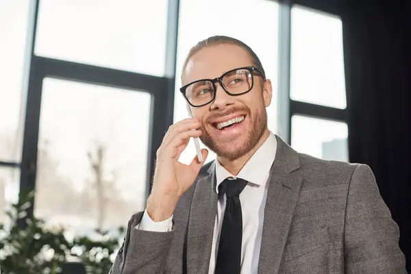 Happy businessman in eyeglasses smiling during conversation on smartphone in office, portrait — Stock Photo