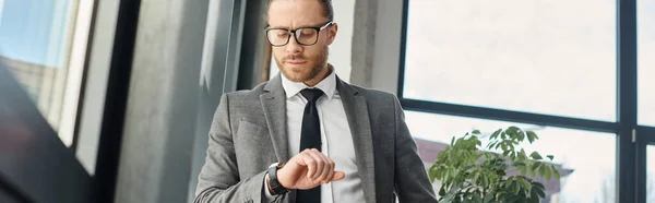 Entrepreneur sérieux en costume et lunettes regardant montre-bracelet dans le bureau, bannière horizontale — Photo de stock