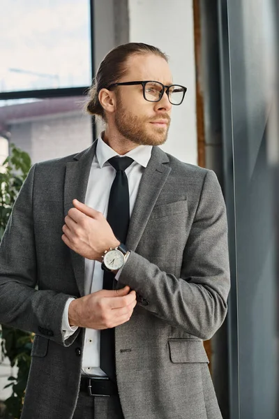 Serious and confident businessman in grey suit and eyeglasses standing and looking away in office — Stock Photo